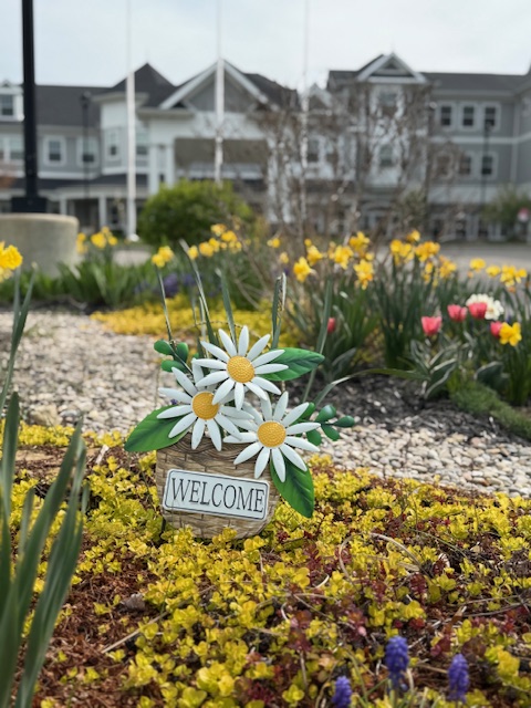 Welcome sign with decorative daisies in garden in front of community living building.